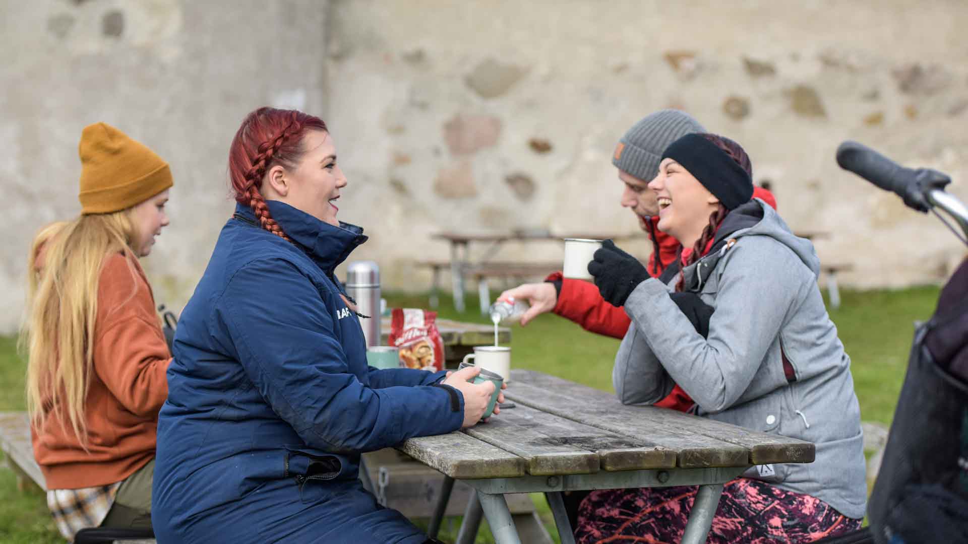 Fyra personer fikar och skrattar vid ett bänkbord utanför Lillöborgen. Foto Jennie Ahlqvist