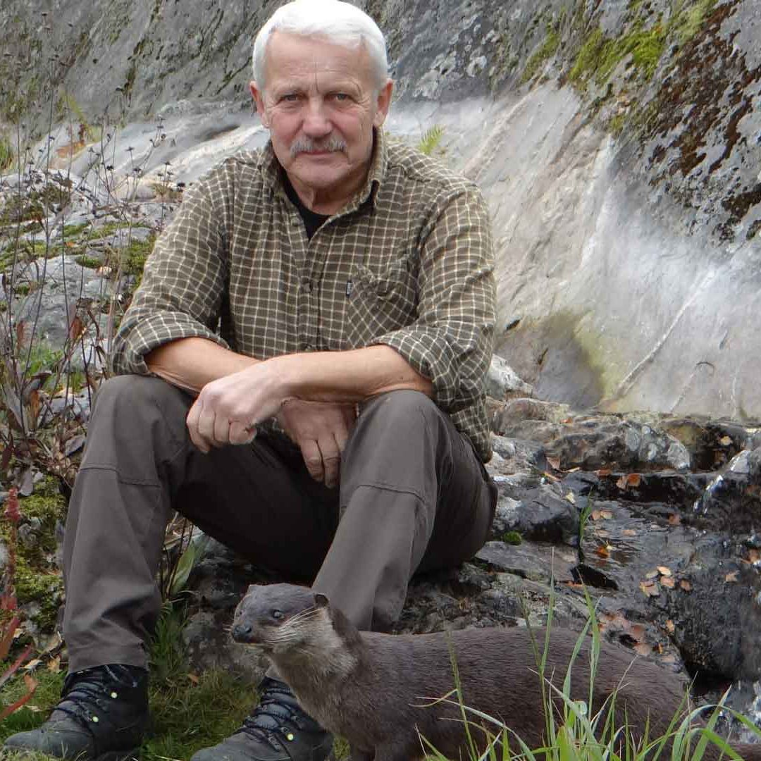 En man sitter på en sten med en uppstoppad utter vid fötterna.