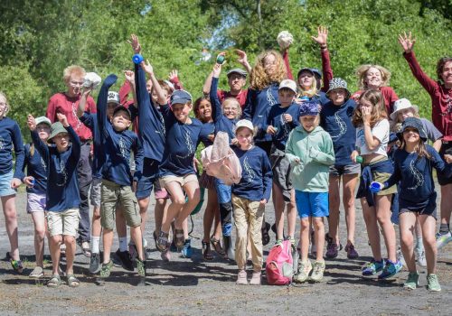 En stor grupp barn i blå tröjor hoppas med armarna upp i luften. Foto Jennie Ahlqvist
