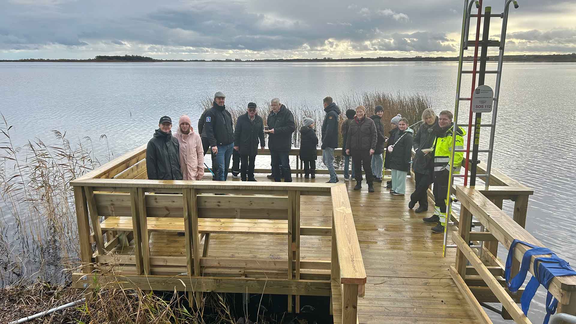 Folk står på fiskebryggan vid Hammarslundsvallen. I bakgrunden syns Hammarsjön. Foto Åsa Pearce.